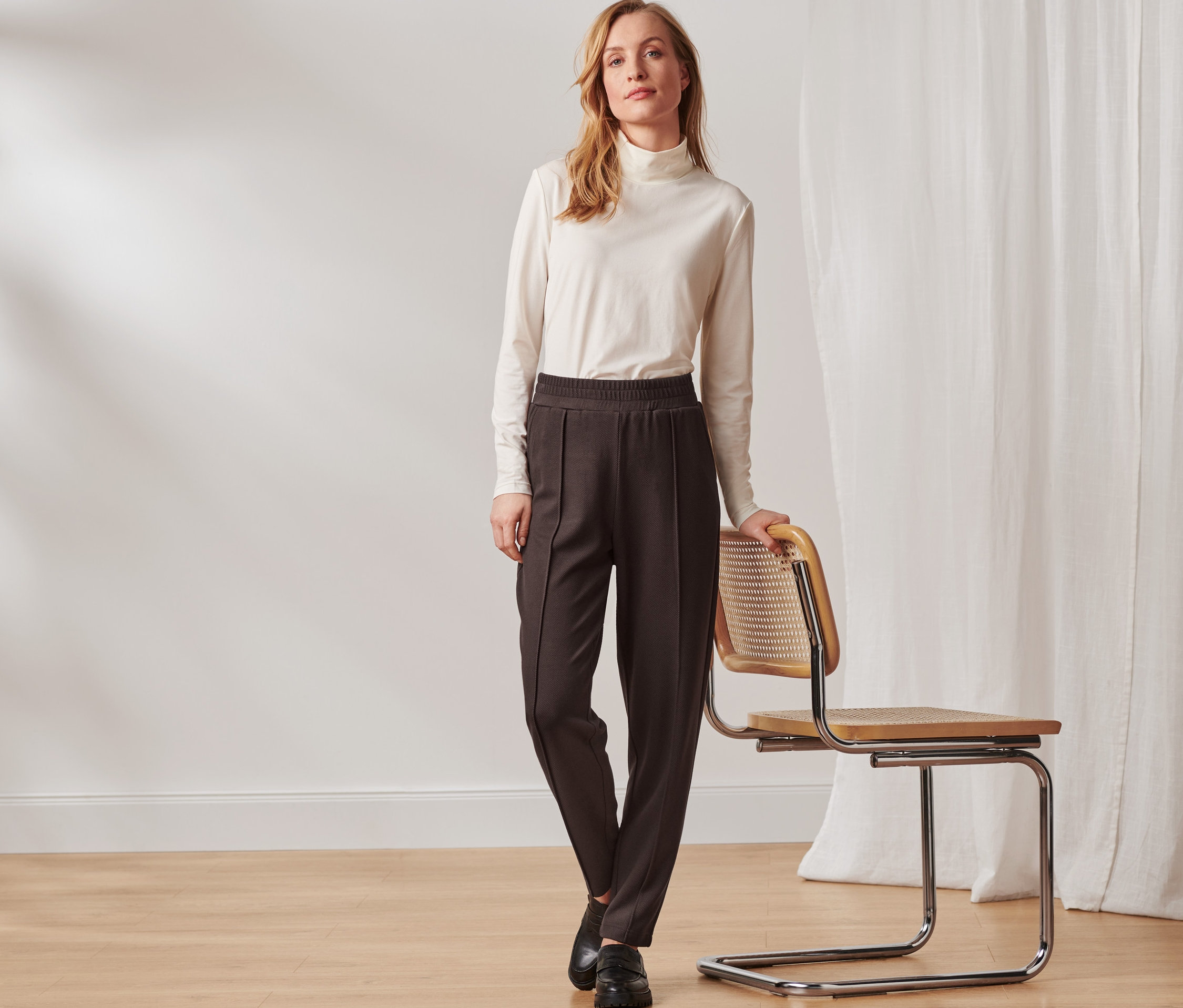 Frau posiert neben einem Stuhl und trägt eine dunkelbraune Joggpants mit Biese.