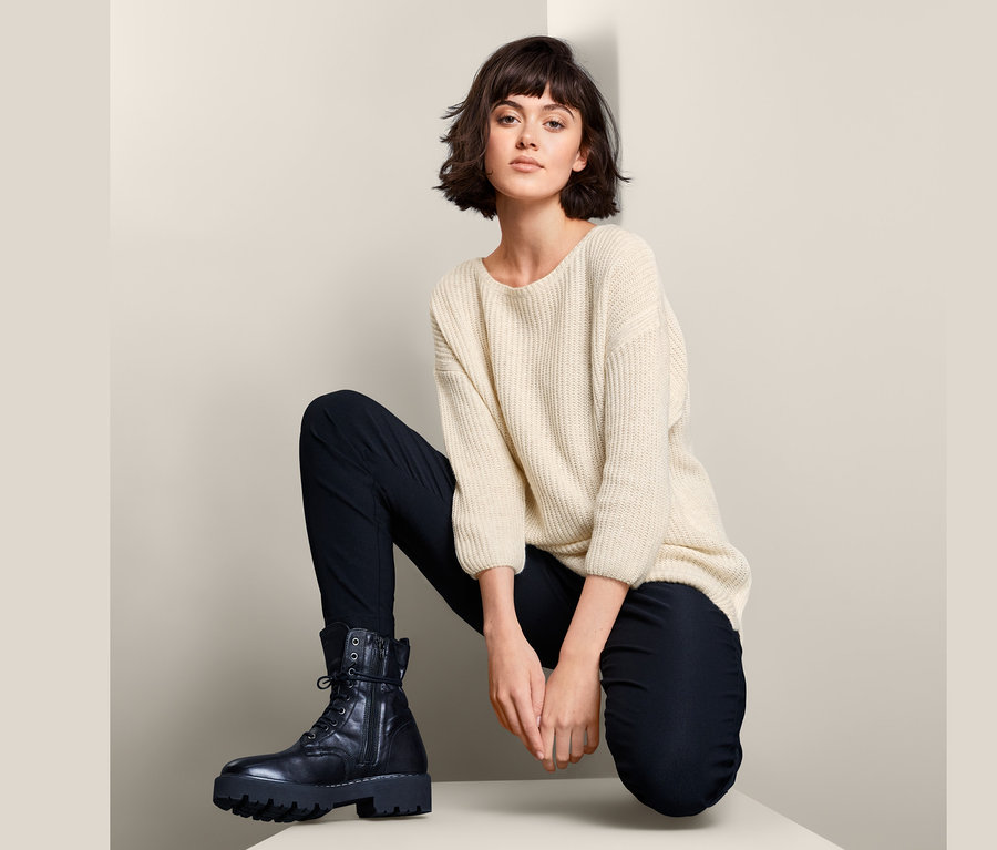 Frau posiert in einem Strickpullover, schwarzen Hosen und Stiefeln.