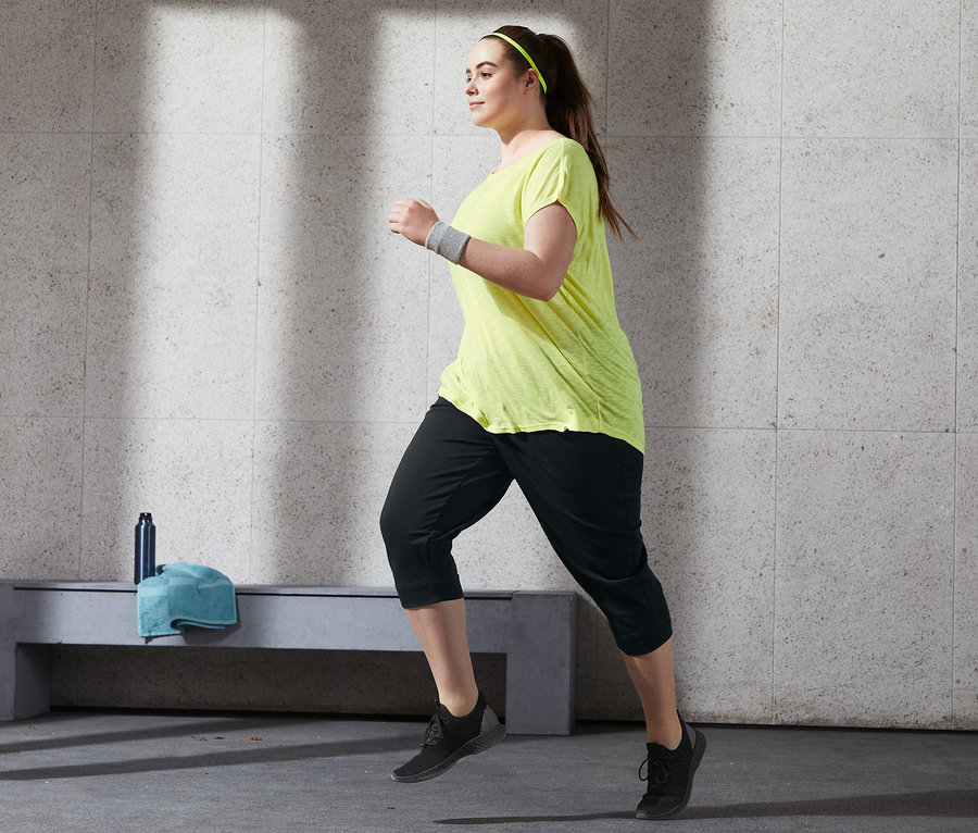 Frau in gelbem Sportshirt und 3/4-Sporthose beim Laufen.