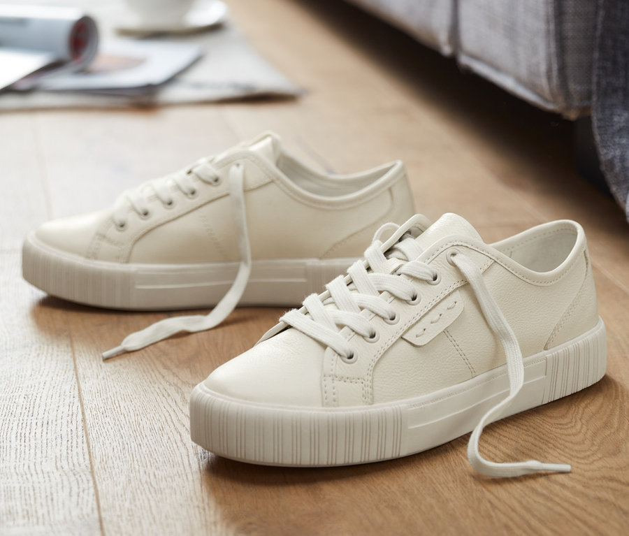 Zwei Leder-Sneaker liegen auf einem Holzboden, im Hintergrund ein Sofa.
