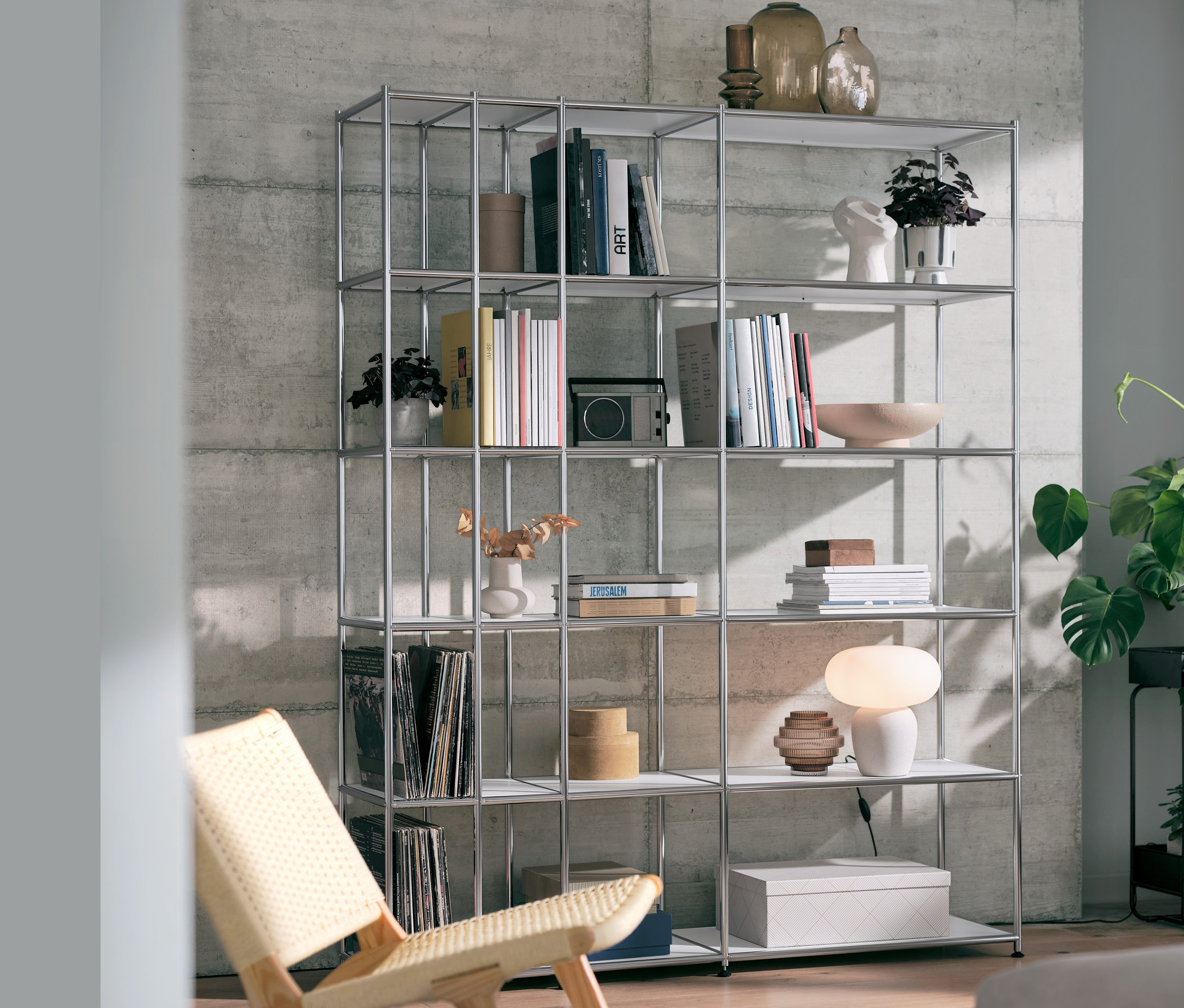 Ein offenes Regal Metall »CN3« in Weiß mit einer Tischleuchte mit Glasschirm und einem Relaxstuhl.