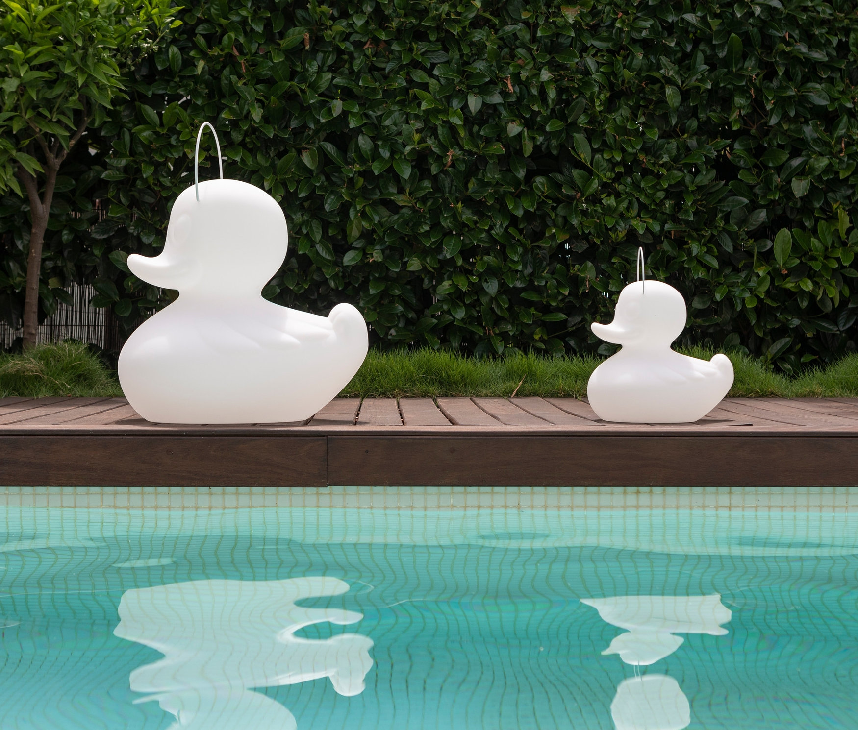 Zwei weiße Goodnight Light LED-Leuchten »Ente« stehen auf einer Holzterrasse an einem Pool.