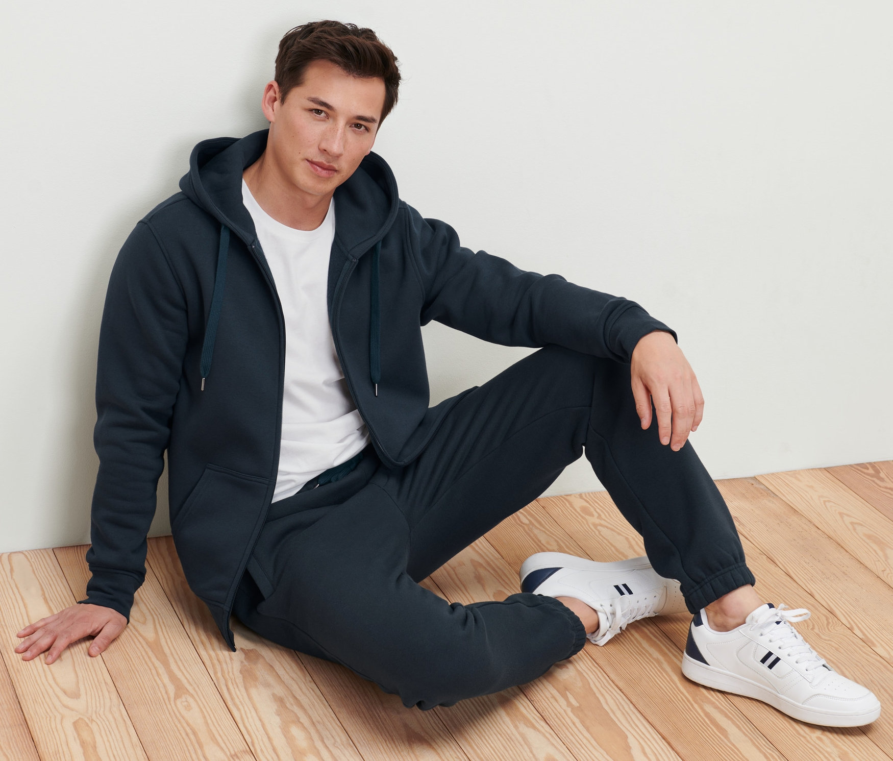 Mann sitzt auf dem Boden und trägt eine Kapuzenjacke.