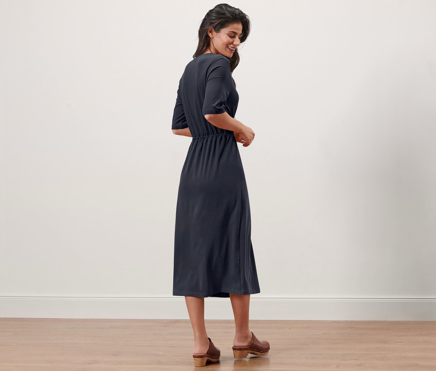 Frau steht seitlich und lächelt, sie trägt ein marineblaues Jerseykleid.