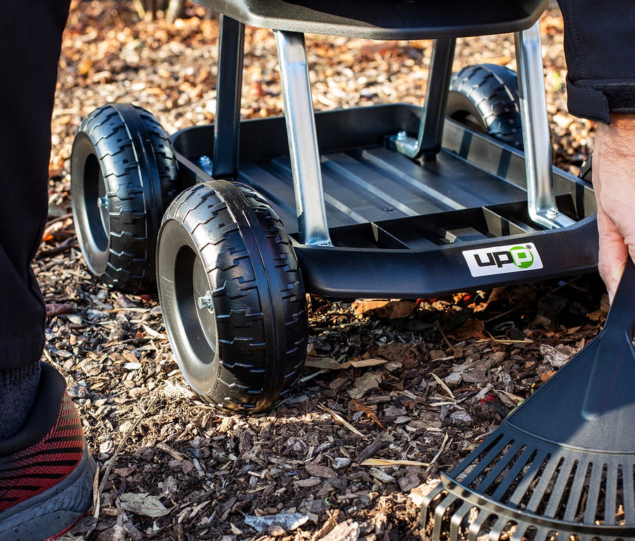 Mann benutzt Rechen neben schwarzem Rollsitz-Gartenwagen.