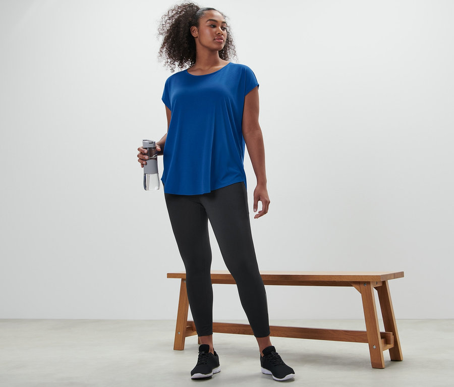 Frau hält eine Wasserflasche und trägt ein blaues Sportshirt und eine schwarze Sporttight.