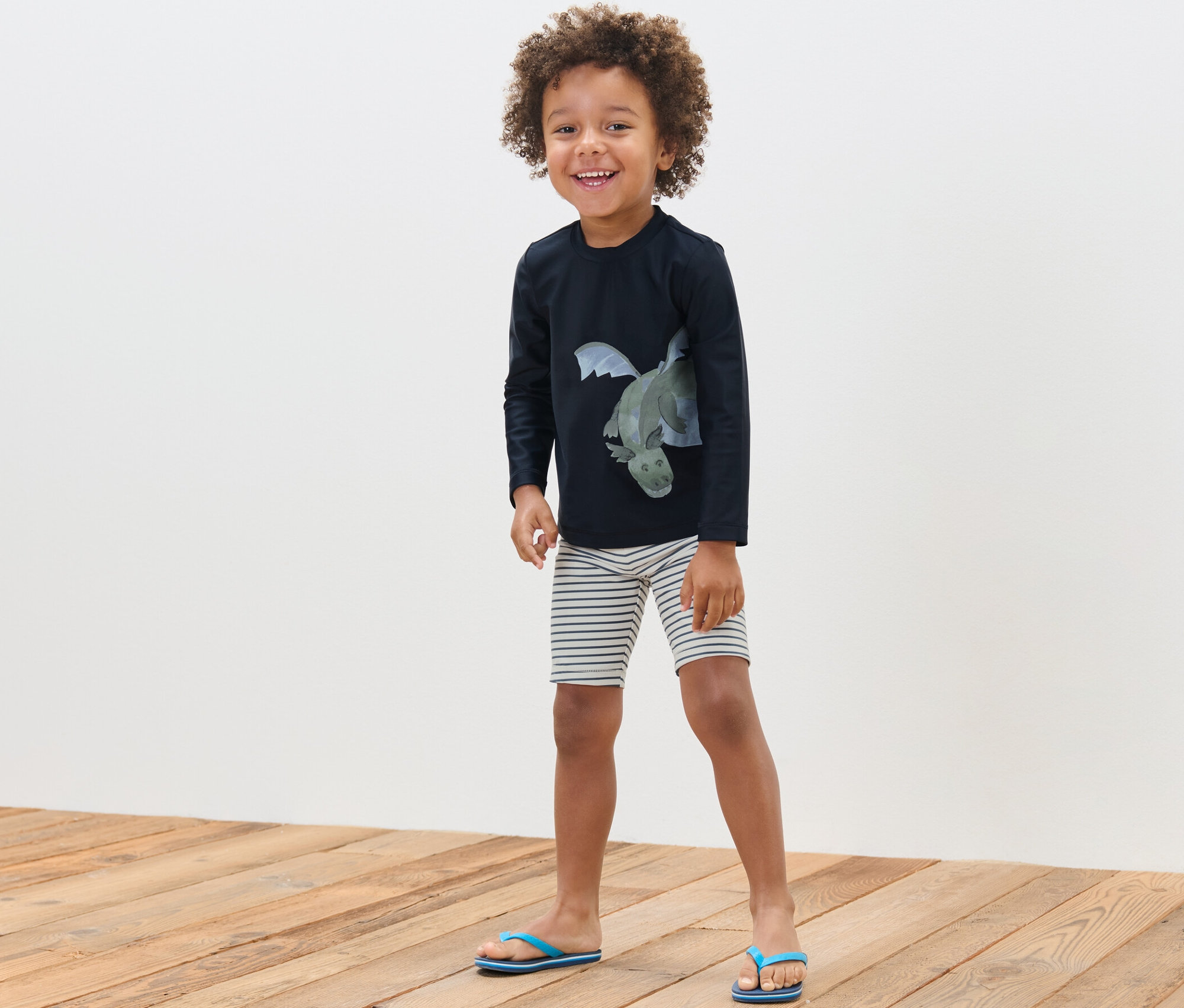 Ein lächelnder Junge posiert in einer Kinder-Kombi mit UV-Schutzfaktor 80, Drache.