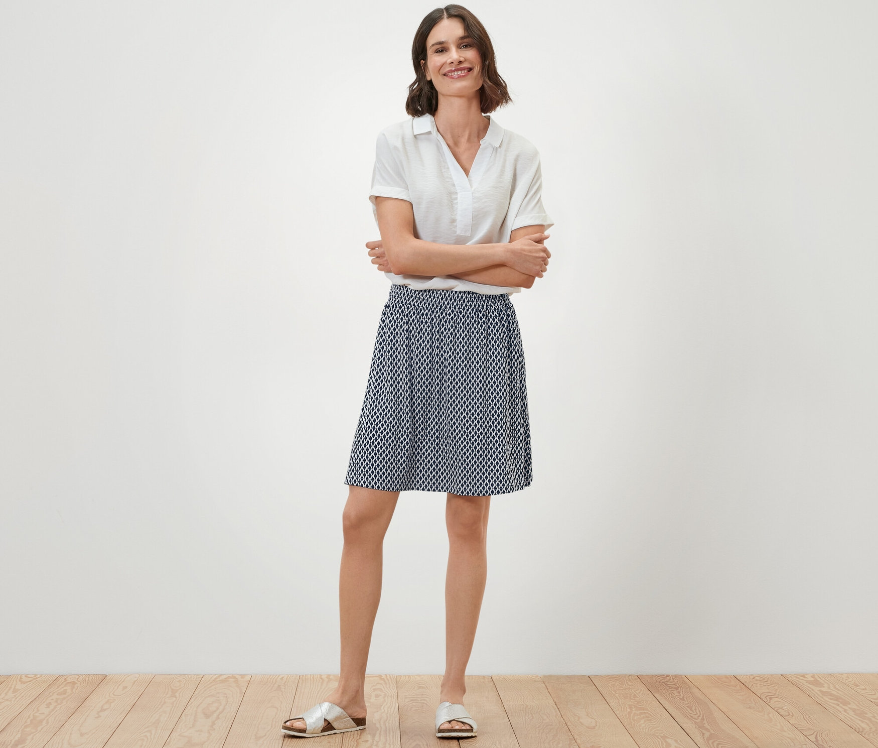 Frau steht mit verschränkten Armen da und trägt einen bedruckten Jerseyrock.