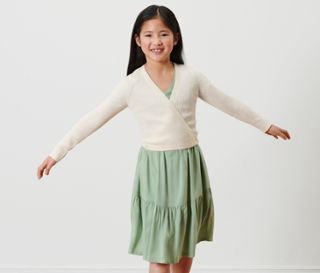 Ein lächelndes Mädchen posiert in einer Kinder-Strickjacke.