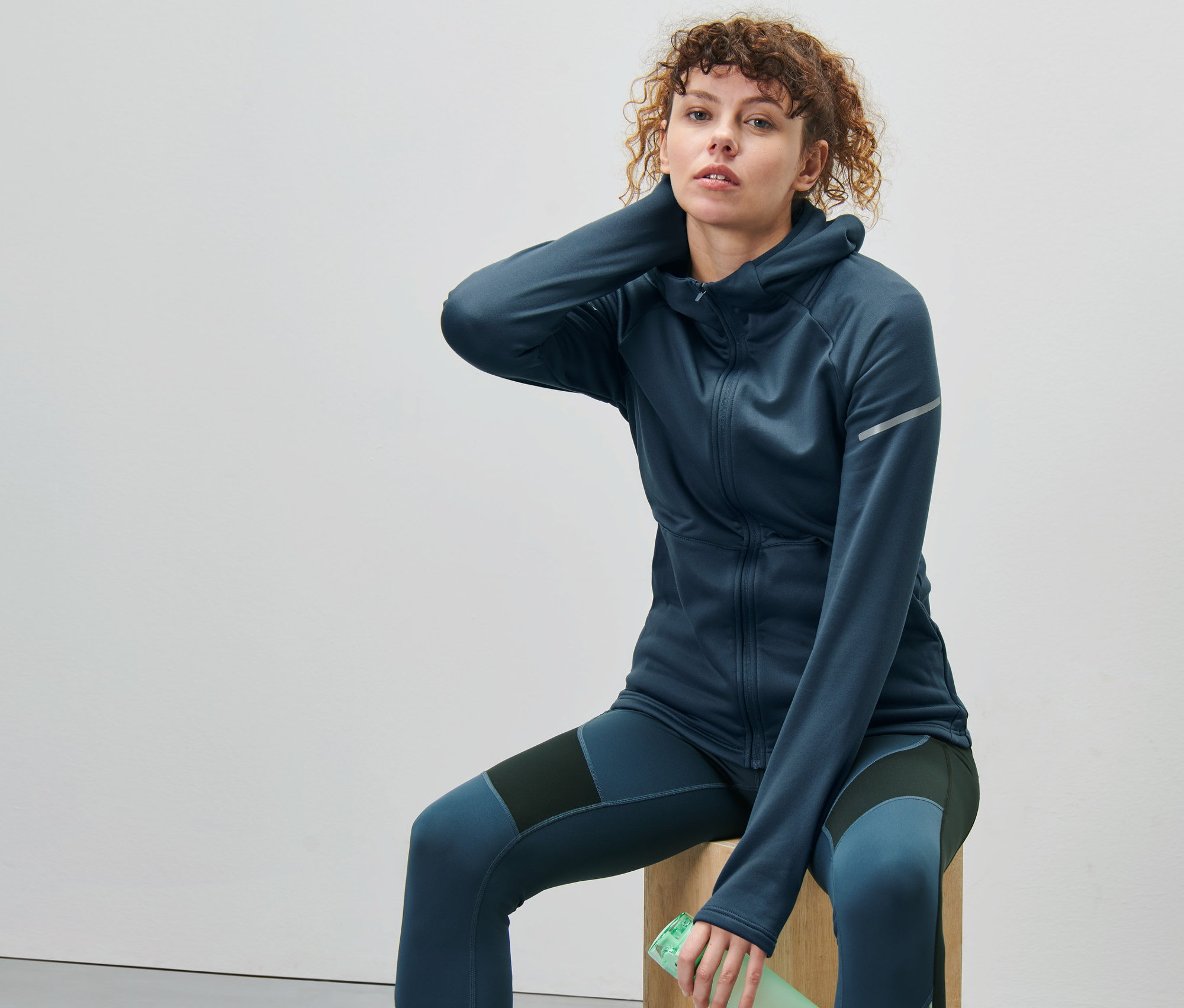 Frau sitzt auf Holzwürfel, trägt dunkelblaue Thermojacke.