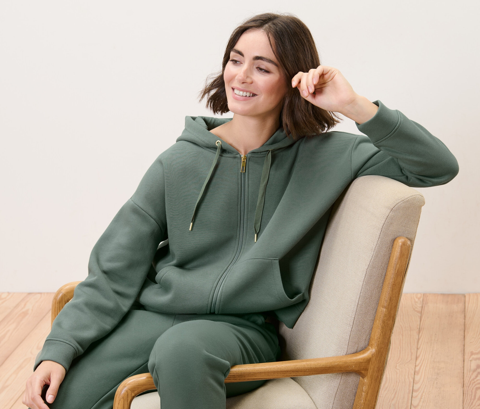 Frau sitzt im Sessel und trägt eine Lounge-Jacke.