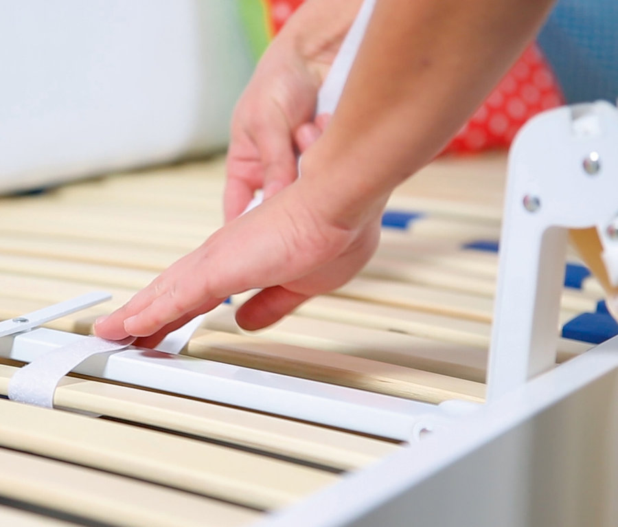 Eine Hand montiert das beige roba Bettschutzgitter »Klipp-Klapp« an einem Lattenrost.
