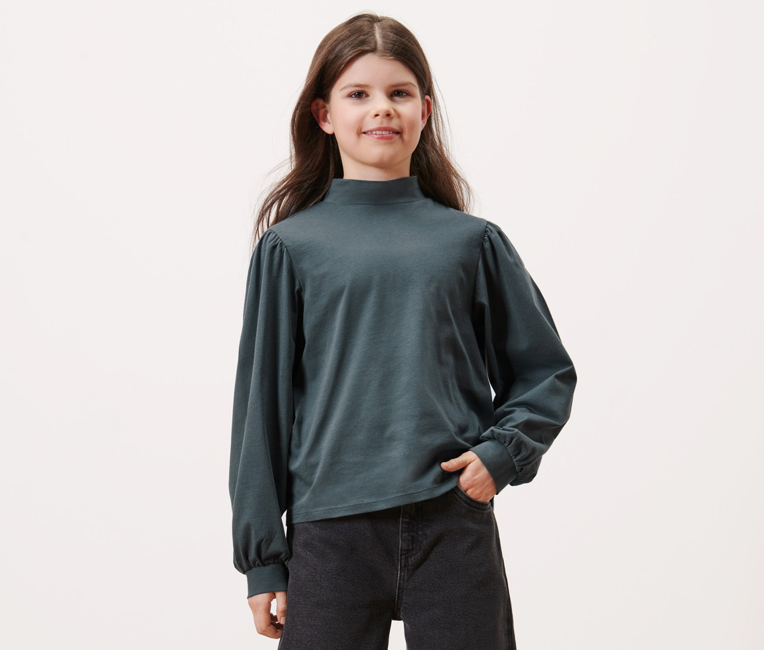 Mädchen posiert in einem Kinder-Langarmshirt, schieferblau, und schwarzen Jeans.