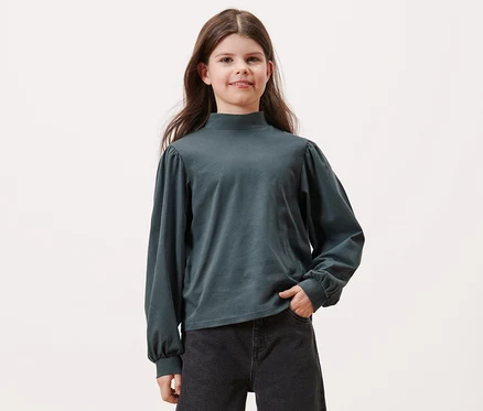Mädchen posiert in einem Kinder-Langarmshirt, schieferblau, und schwarzen Jeans.