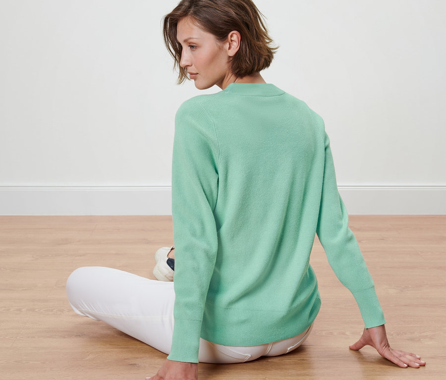 Frau sitzt auf dem Boden und trägt einen Pullover.