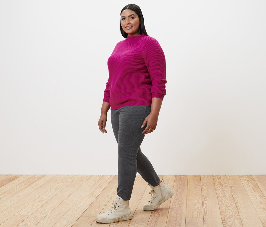 Frau geht und trägt einen pinken Strickpullover mit Stehkragen, Joggpants und gefütterte Leder-Sneaker.