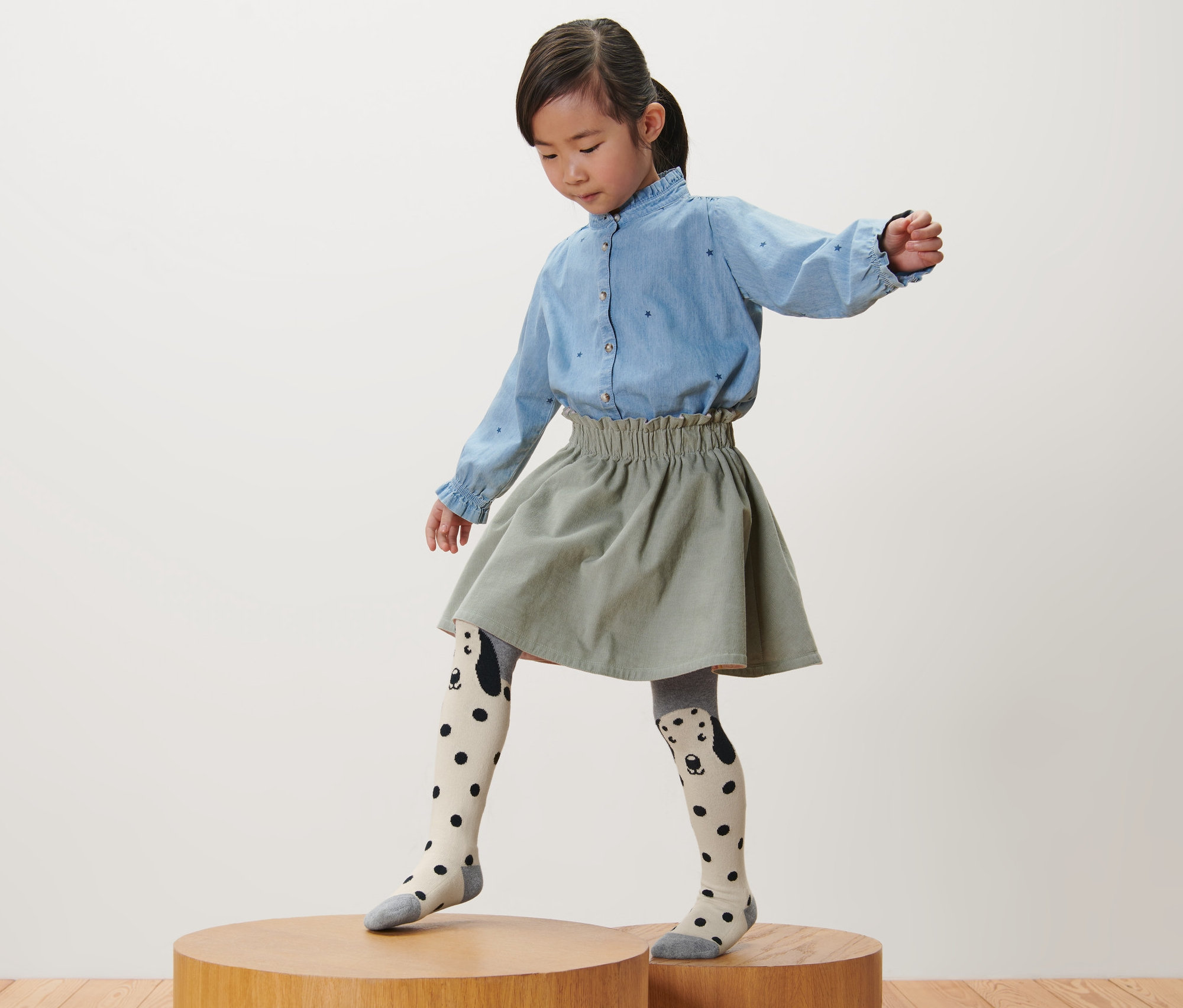 Mädchen steht auf einem Holzsockel und trägt 3 Kinder-Strumpfhosen, rosa, grau, beere.
