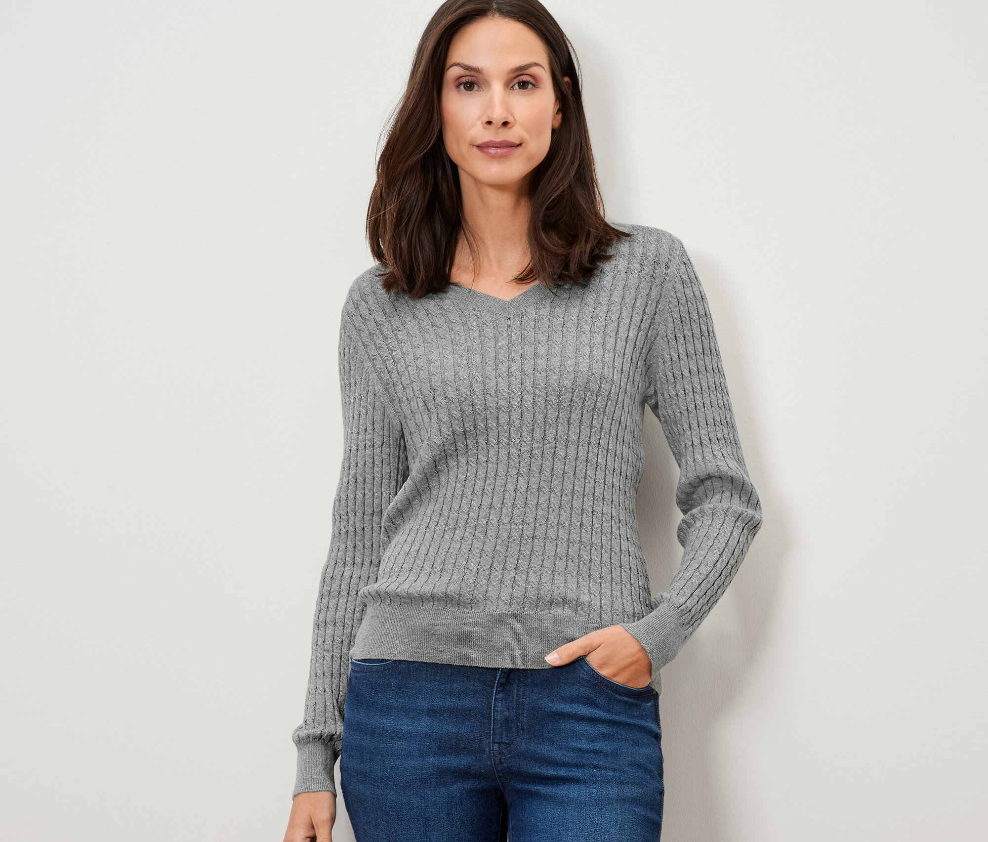 Frau posiert in grauem Zopfstrickpullover und blauen Jeans.
