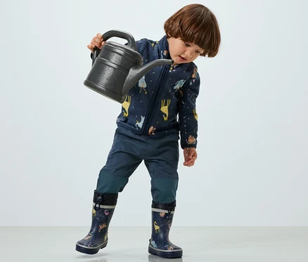 Ein Kind hält eine Gießkanne und trägt eine Kinder-Outdoorhose.