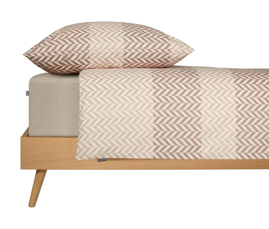 Bett mit beigem Spannbettlaken und Kissen mit grauem Fischgrätenmuster.
