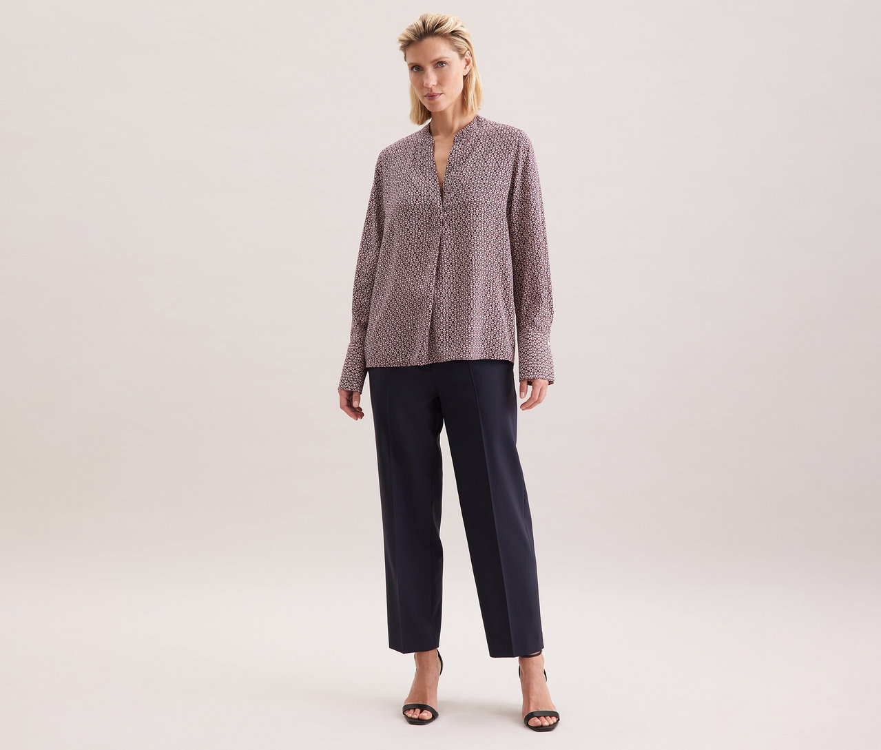 Frau trägt eine Seidensticker Tunika aus Viskose mit ecru-burgundy Alloverprint, kombiniert mit dunklen Hosen und schwarzen Sandalen.