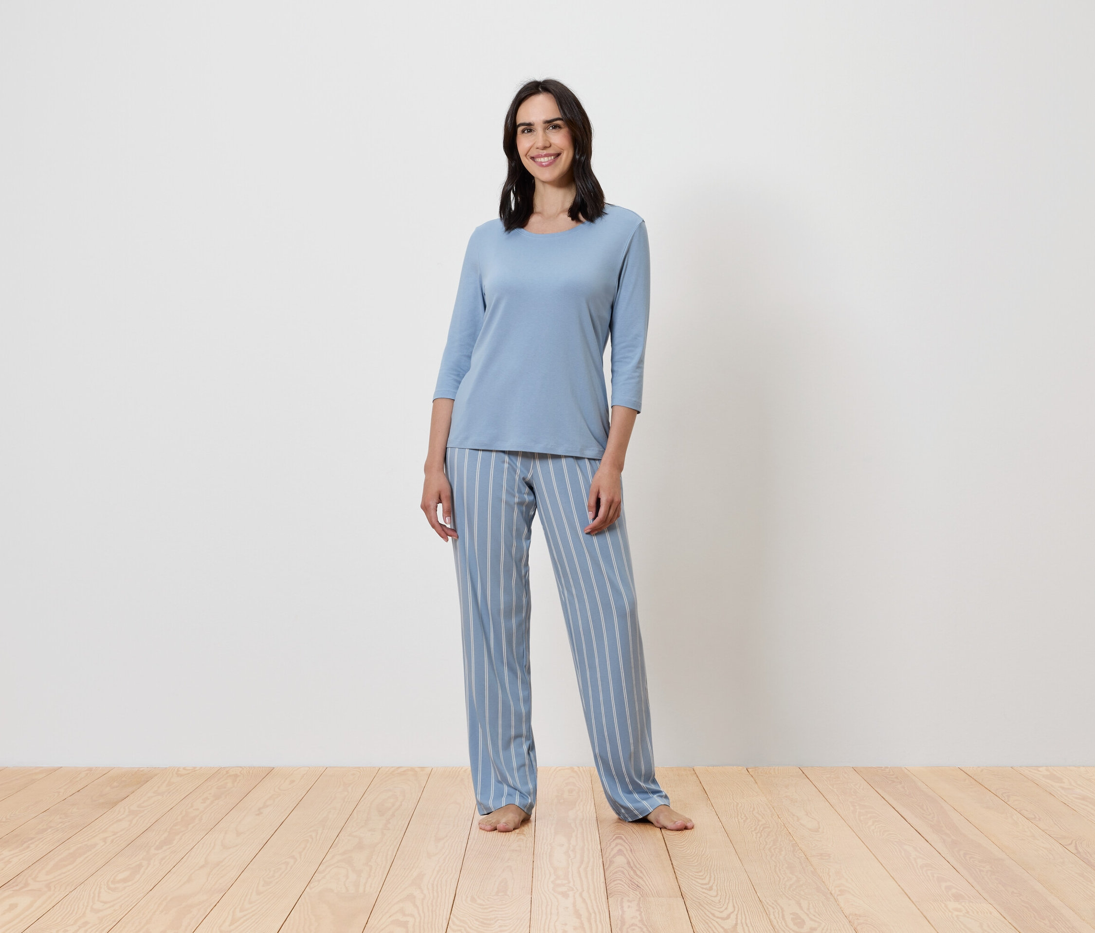 Frau steht und trägt einen blauen, gestreiften Pyjama.