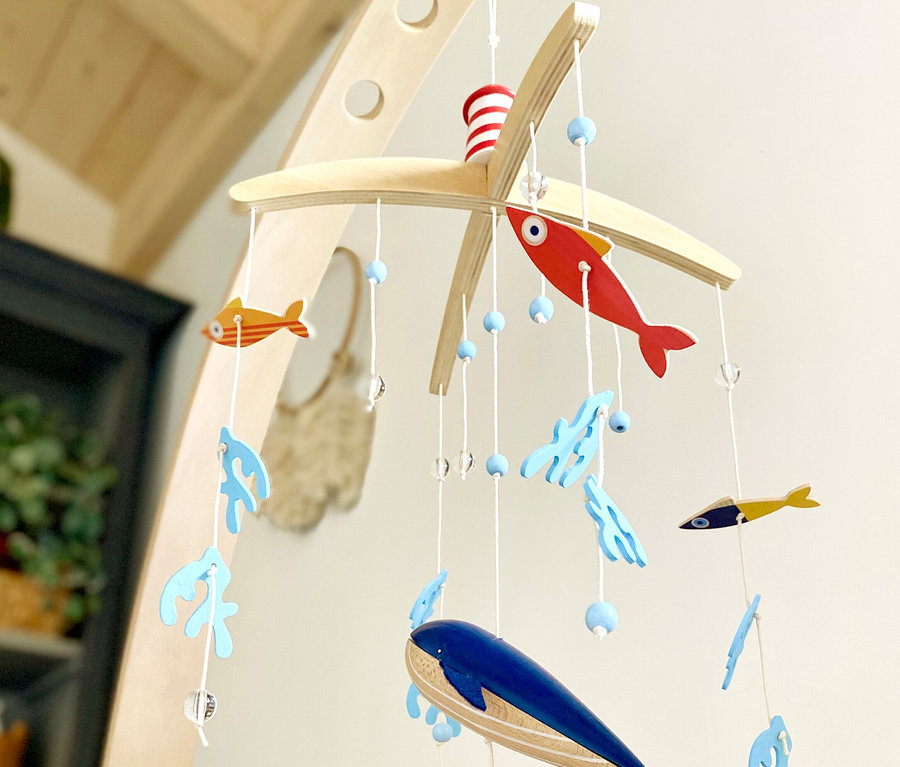 Ein Babymobile mit Holzfischen, Wal und Korallen hängt über einem Kinderbett. small foot Mobile mit Halterung »Seaside«.