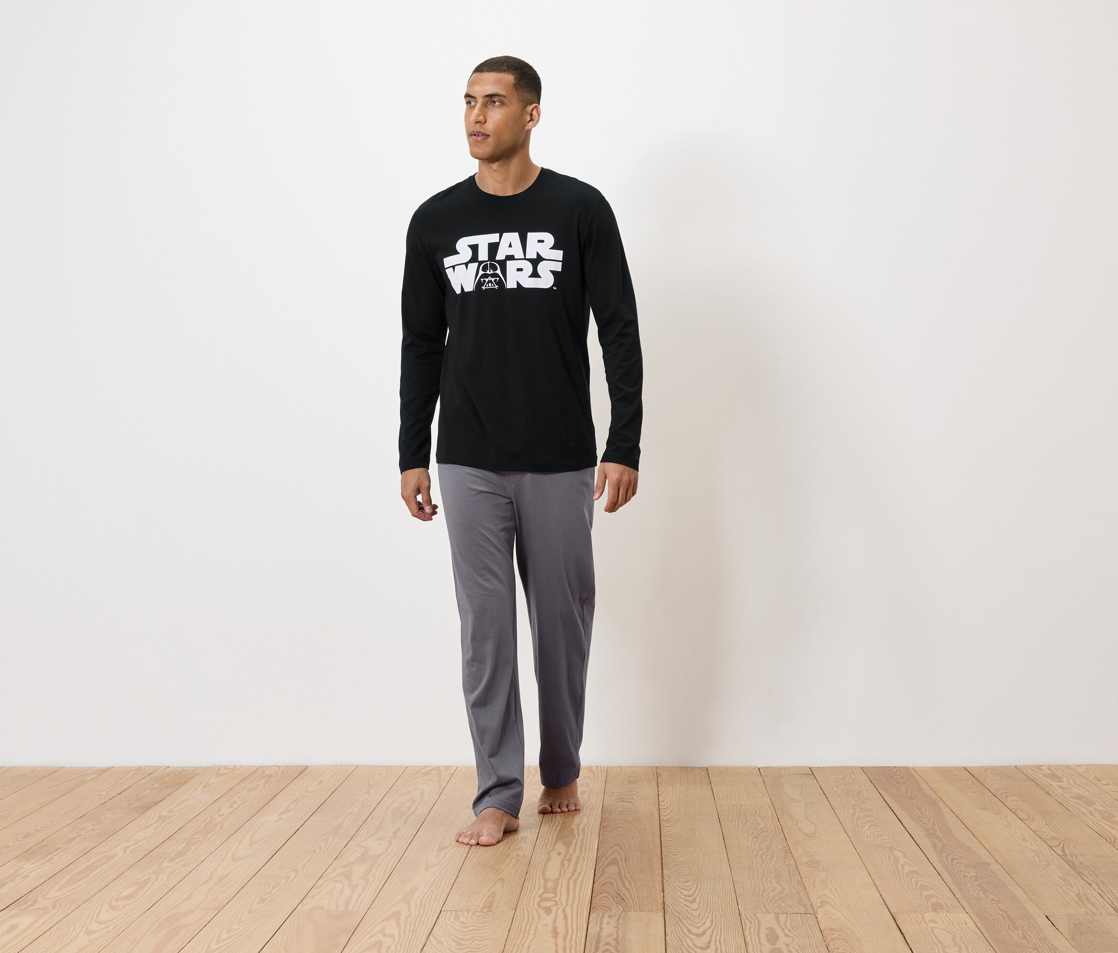 Mann steht barfuß auf einem Holzboden und trägt einen schwarzen Star Wars Schlafanzug.