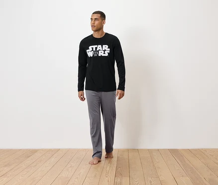 Mann steht barfuß auf einem Holzboden und trägt einen schwarzen Star Wars Schlafanzug.