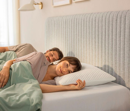Frau liegt im Bett auf einem TEMPUR PRIMA® Schlafkissen Medium, neben ihr schläft ein Mann.