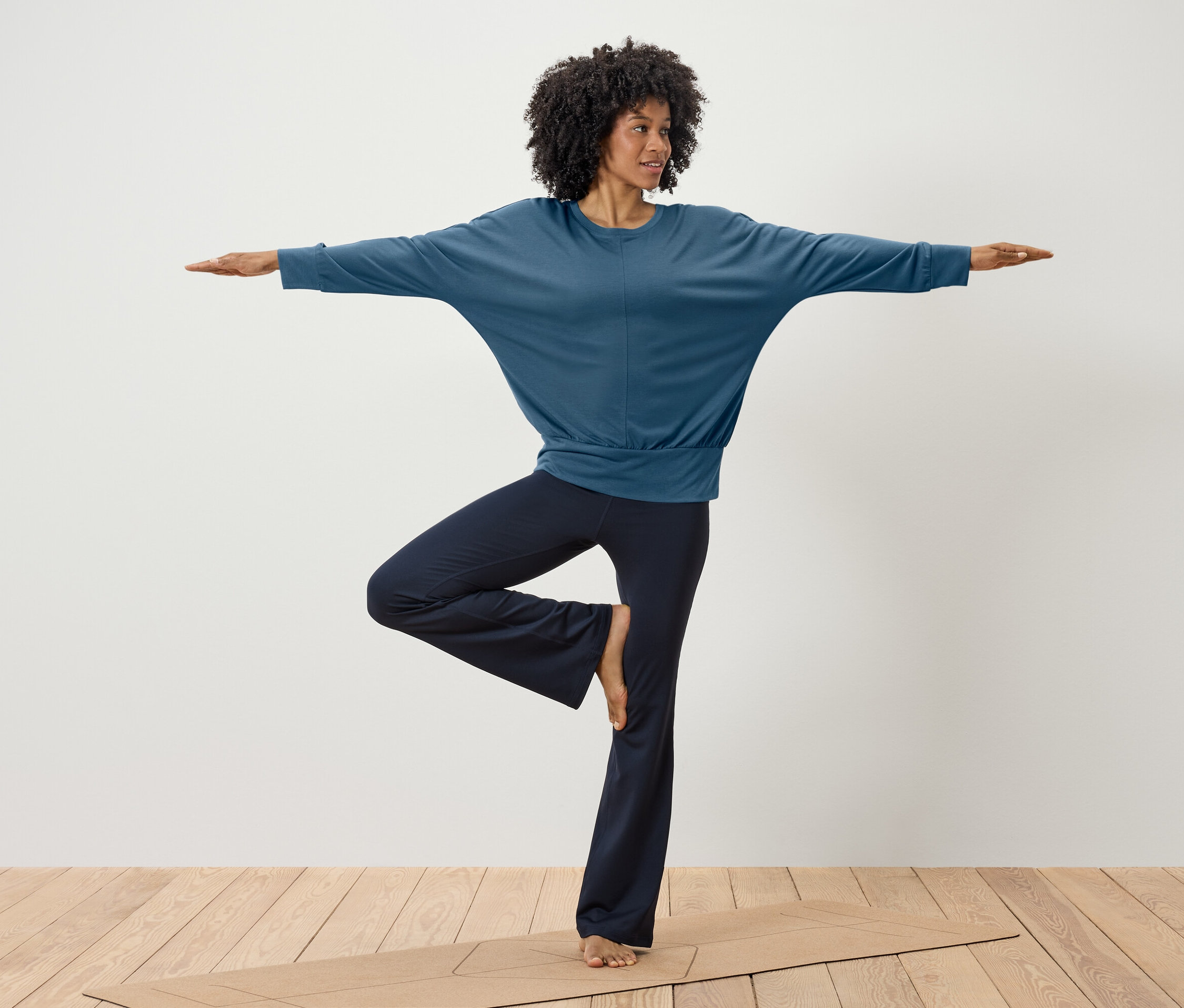 Eine Frau macht Yoga in einem blauen Oberteil und dunkelblauen Hosen auf einer Matte.