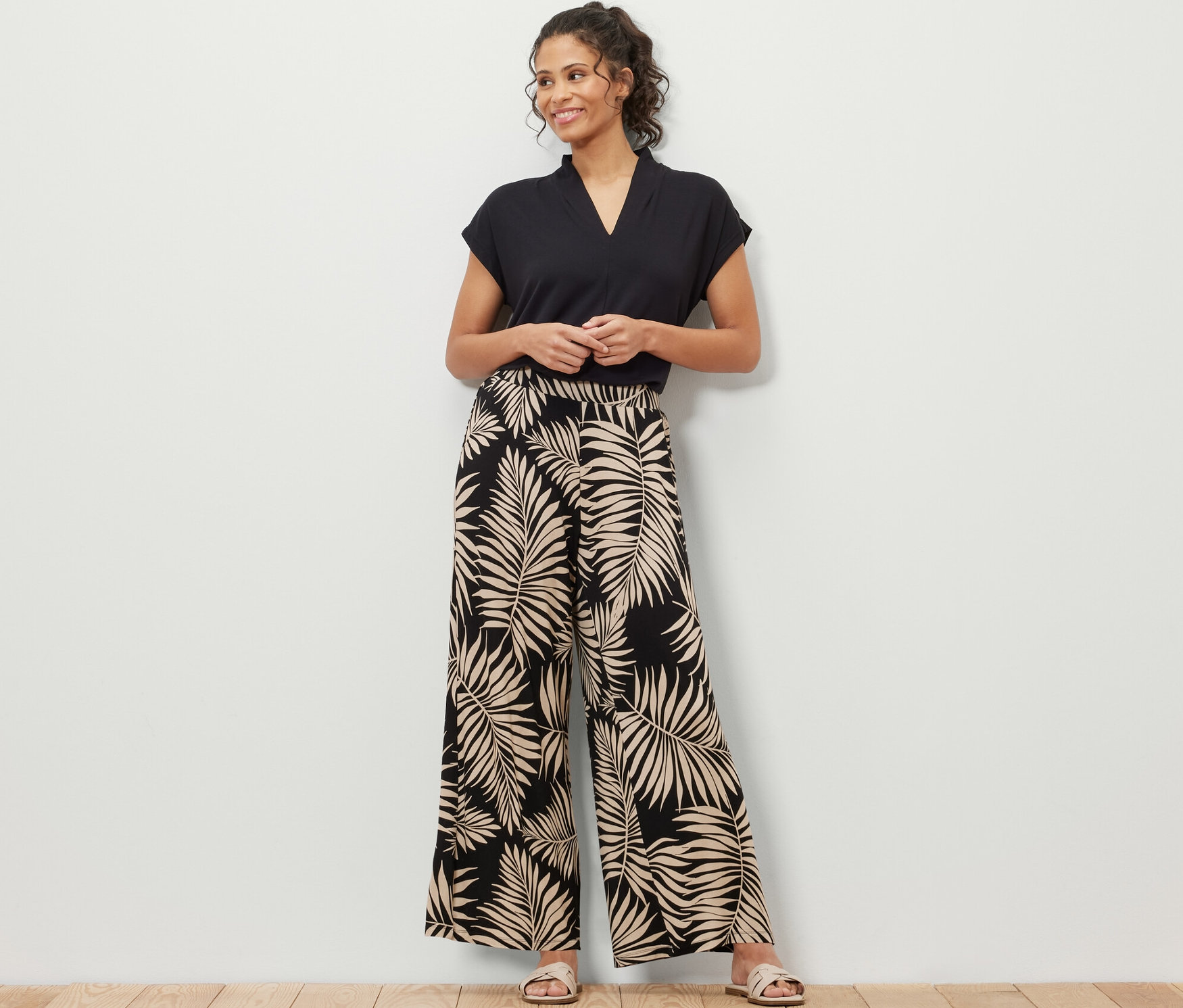 Eine Frau steht und trägt ein schwarzes T-Shirt und eine bedruckte Palazzohose mit Blattmuster.