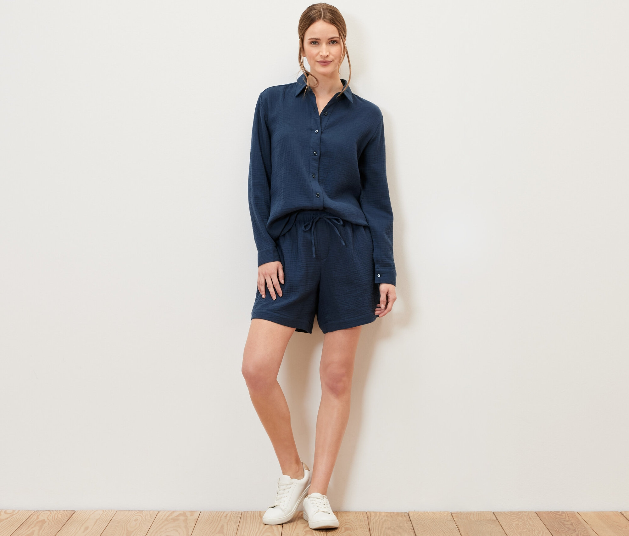 Frau steht und trägt eine marineblaue Musselin-Bluse und Shorts.