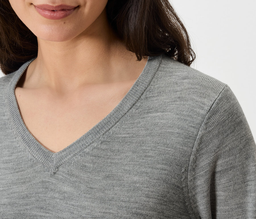 Oberkörper einer Frau in einem grauen Pullover mit V-Ausschnitt.