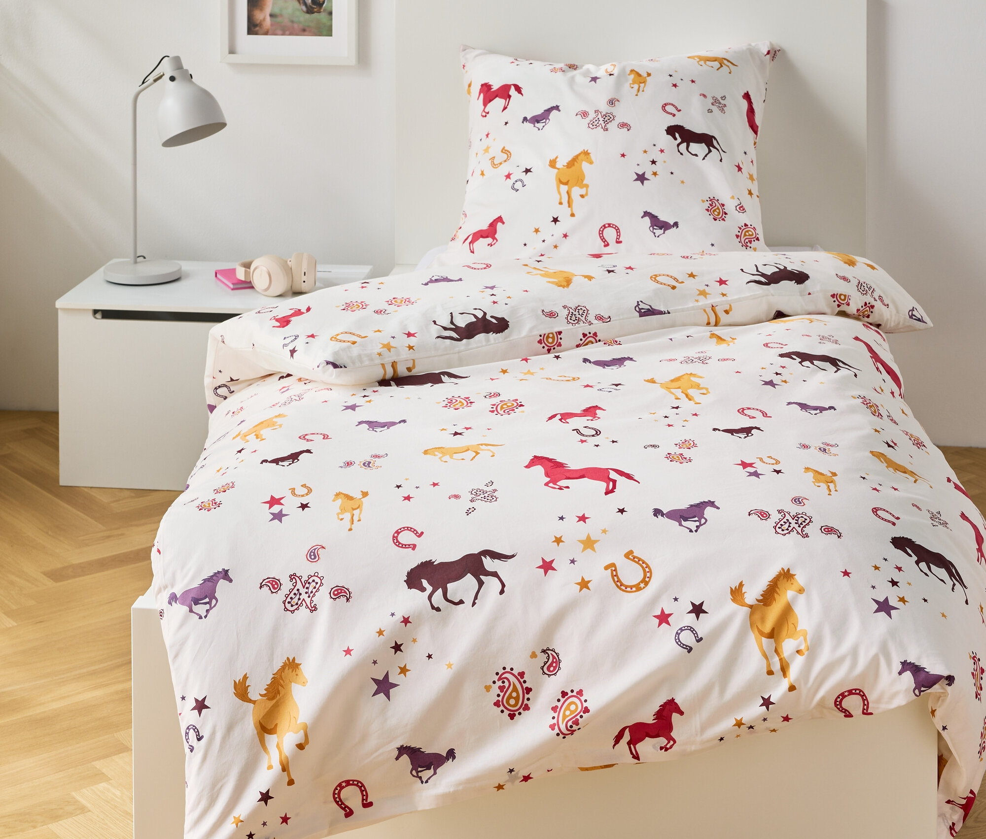Bett mit weißer Bettwäsche mit Pferde-, Hufeisen- und Sternenmuster.
