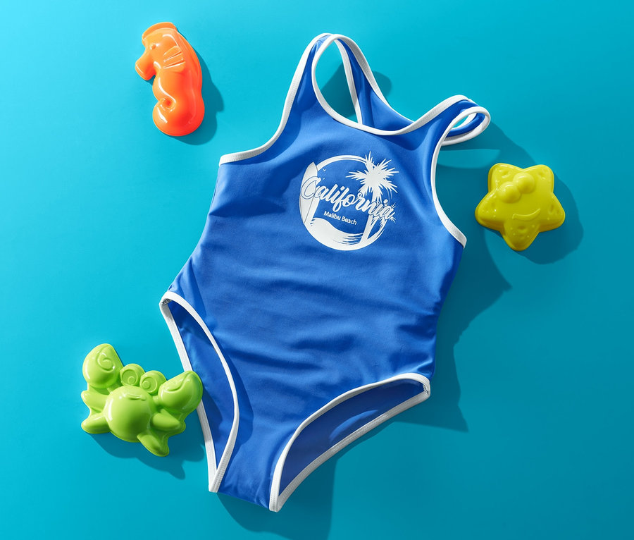 Blauer Badeanzug mit weißen Akzenten und "California" Aufdruck, umgeben von Sandspielzeug auf blauem Hintergrund.