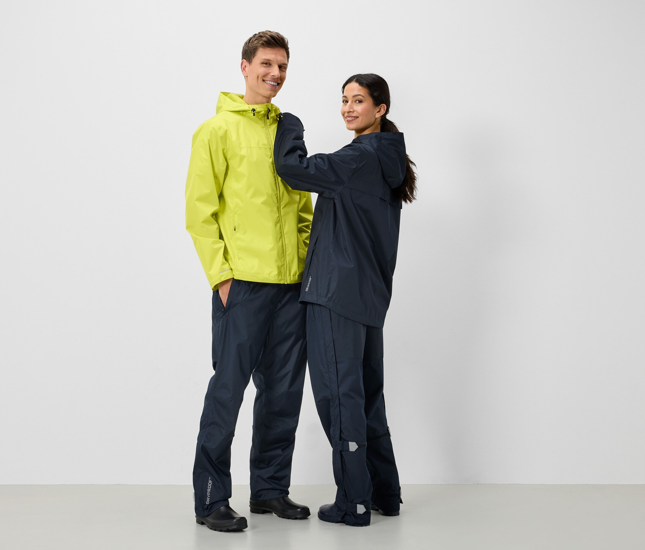 Zwei Personen in Regenjacken und Regenhosen, ein Mann in Gelb und eine Frau in Dunkelblau.
