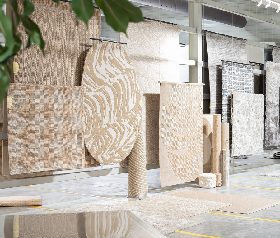 Verschiedene Teppiche hängen und liegen in einem Ausstellungsraum. Darunter ein Woood Teppich »Praline« 200 cm, nougat.