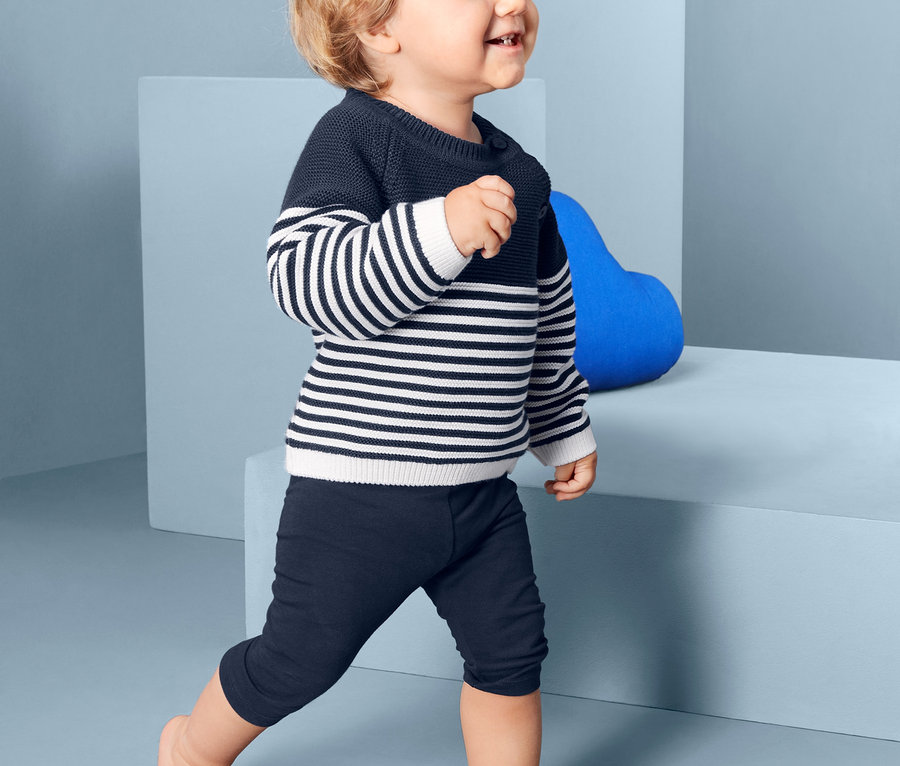 Kleiner Junge geht, trägt blaue 3/4 Leggings aus einem 5er-Set und einen gestreiften Pullover.