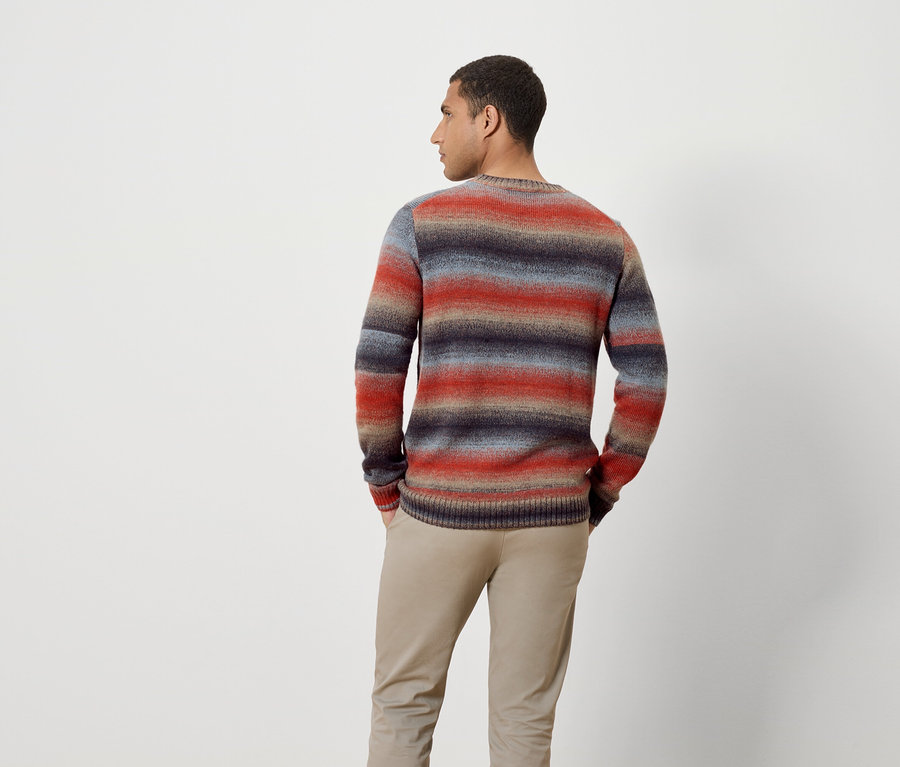 Mann mit dem Rücken zur Kamera trägt einen Streifenpullover und eine Hose.