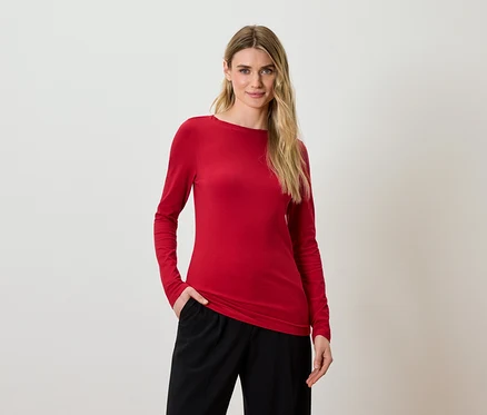 Eine blonde Frau posiert in einem roten Langarmshirt und einer schwarzen Hose.