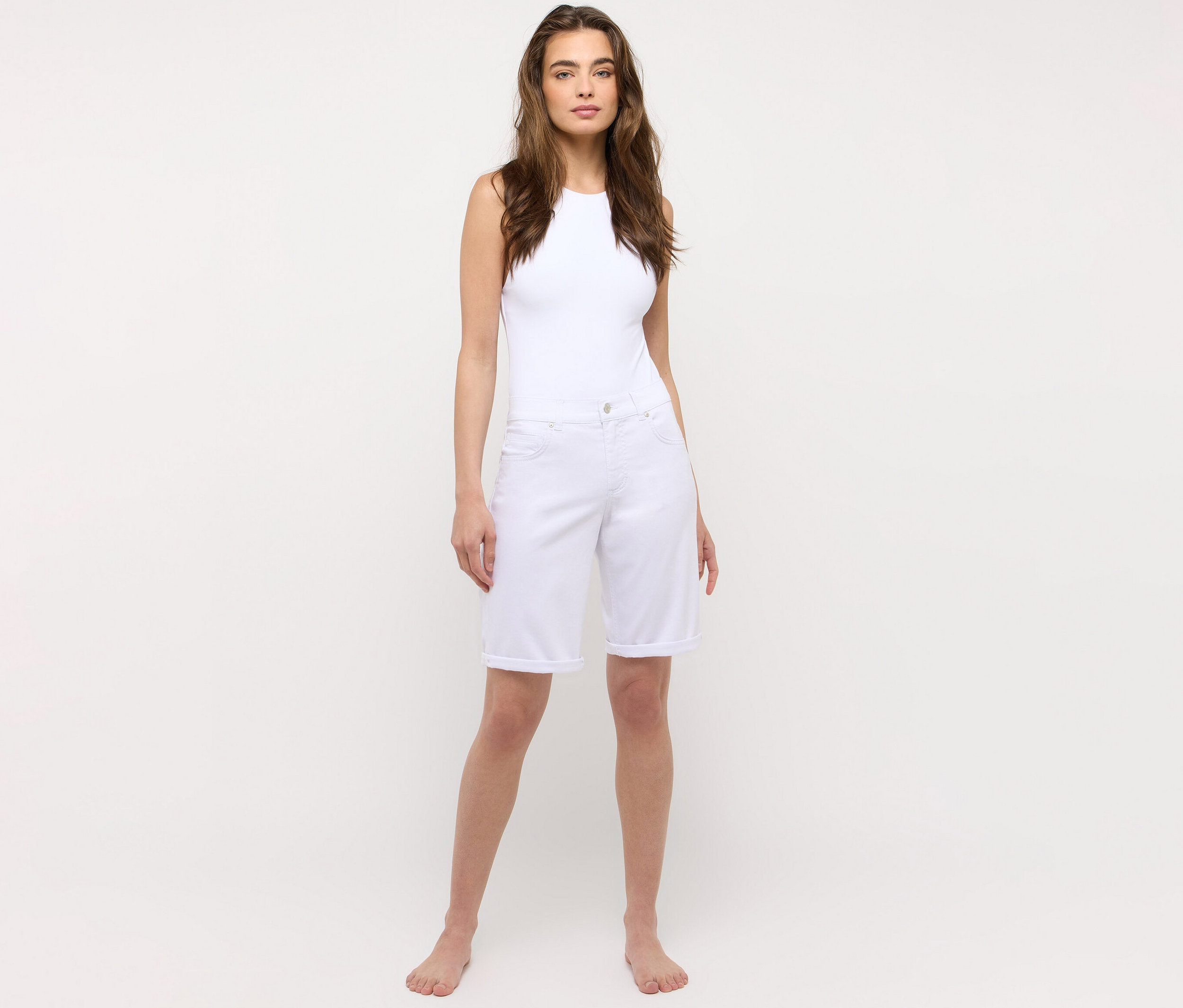 Frau steht barfuß und trägt ein weißes Tanktop und eine weiße Angels Jeans »Bermuda Turn-Up« in Straight Fit.