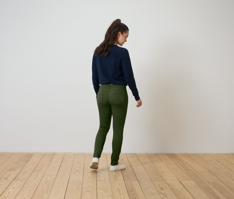 Frau steht mit dem Rücken zur Kamera, trägt einen dunkelblauen Pullover und grüne Jeans.