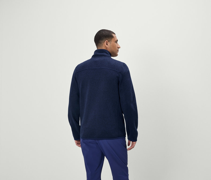 Mann trägt einen blauen Reißverschluss-Pullover und eine blaue Hose.