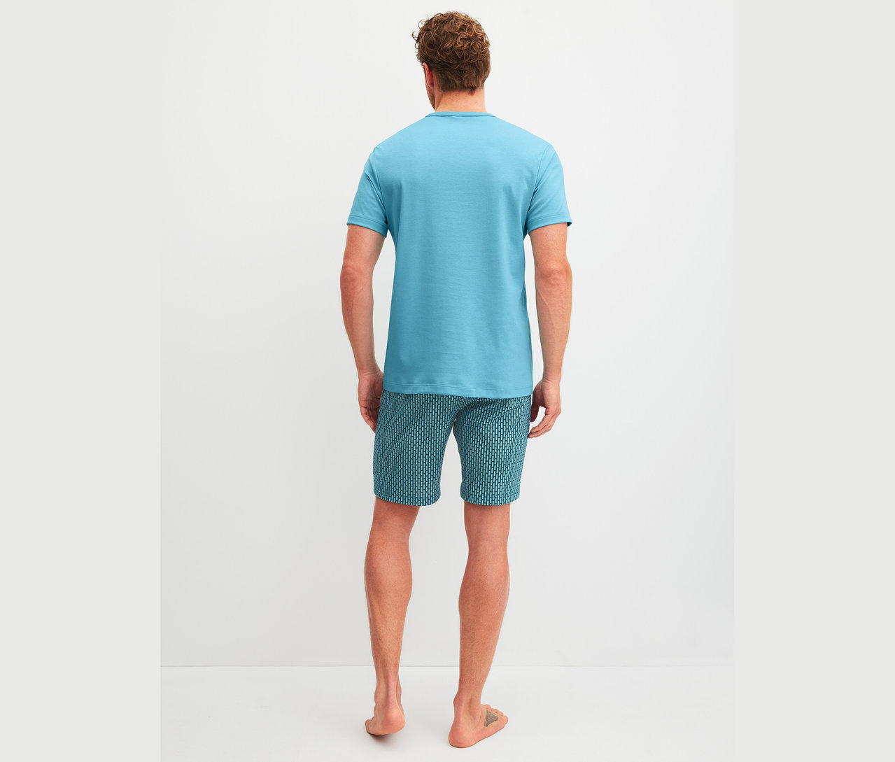 Mann von hinten in blauem T-Shirt und gemusterten Shorts.