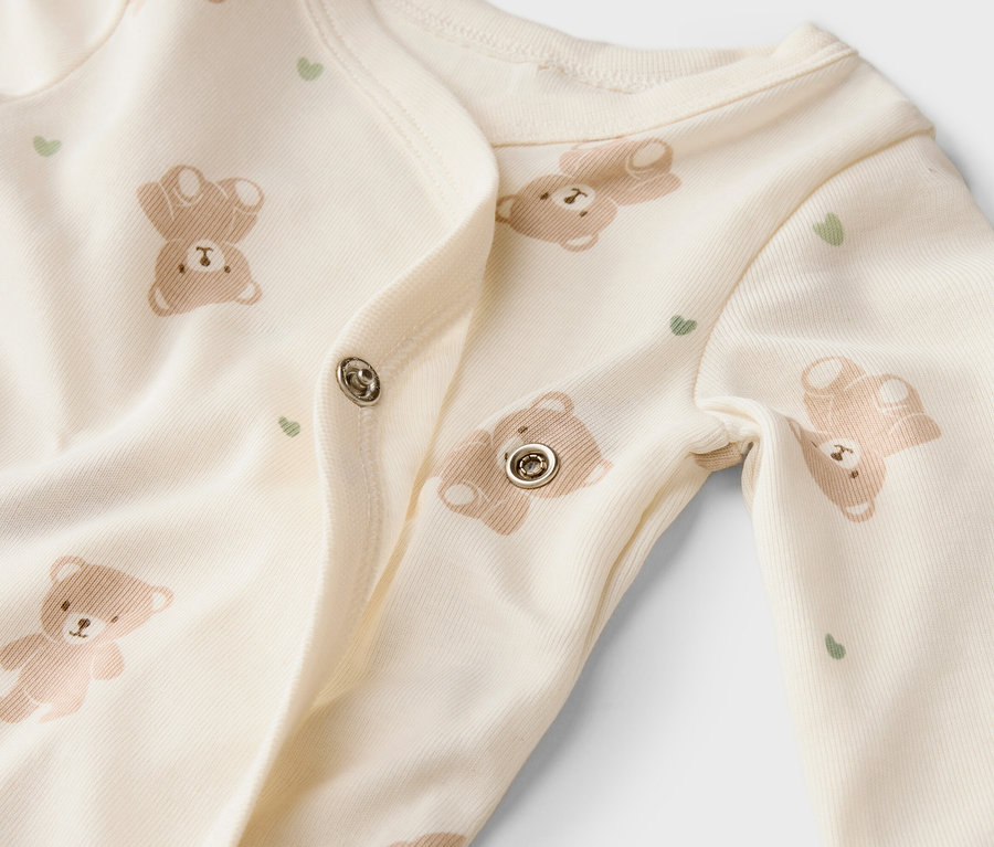 Nahaufnahme eines hellen Baby-Schlafanzugs mit Bären- und Herzmuster und Druckknöpfen.