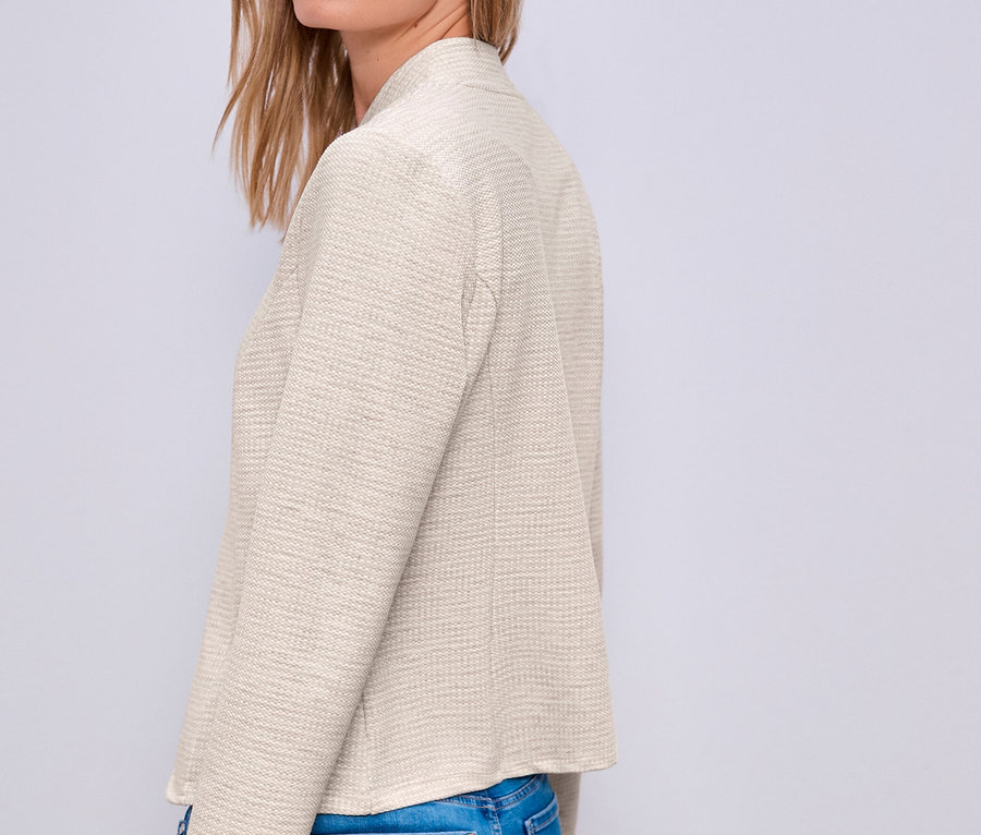 Blonde Frau trägt einen hellen Street One Jerseyblazer und blaue Jeans, blickt über ihre Schulter.