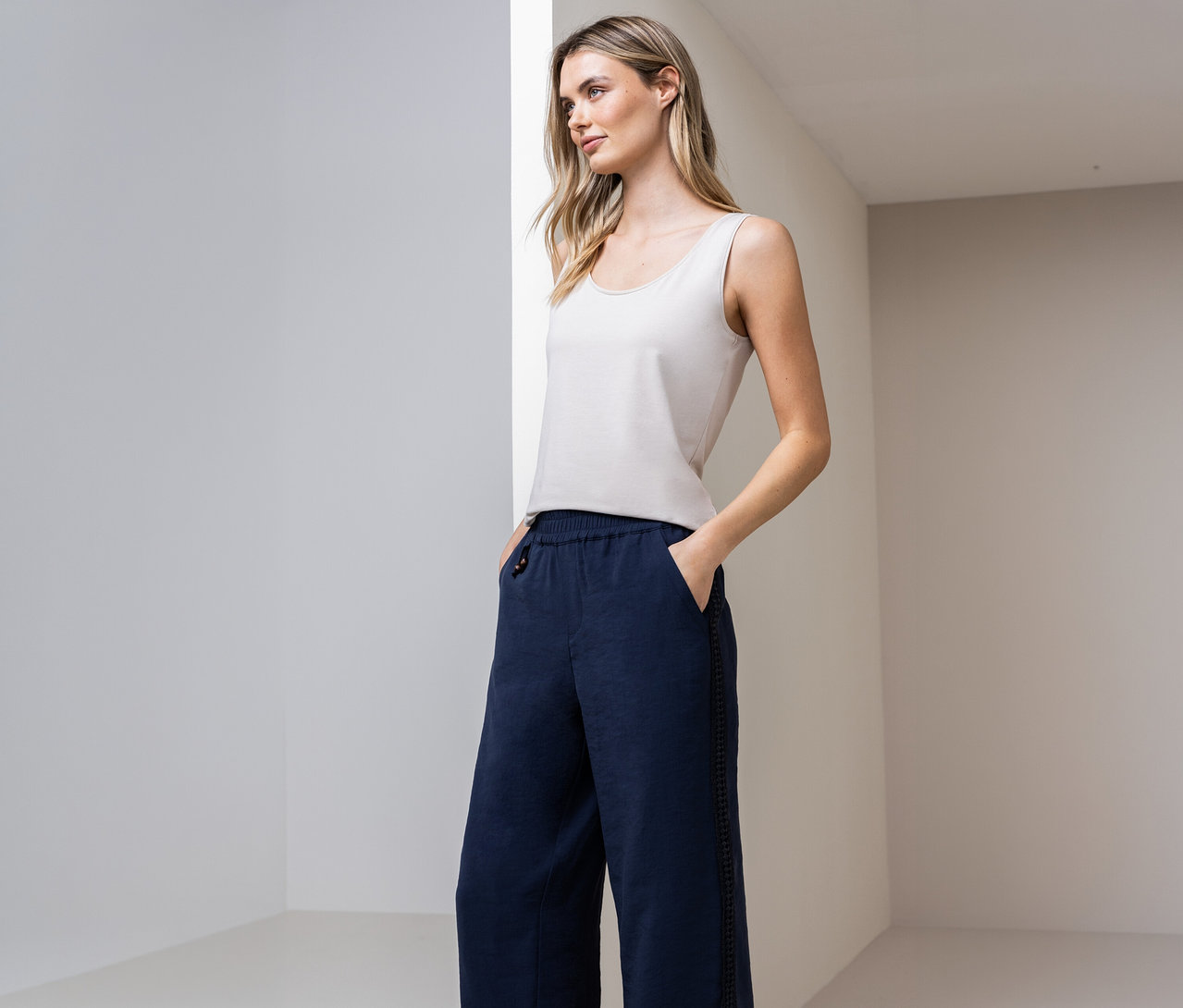 Frau mit Street One Basic-Top und blauer Hose mit Händen in den Taschen vor Wand.