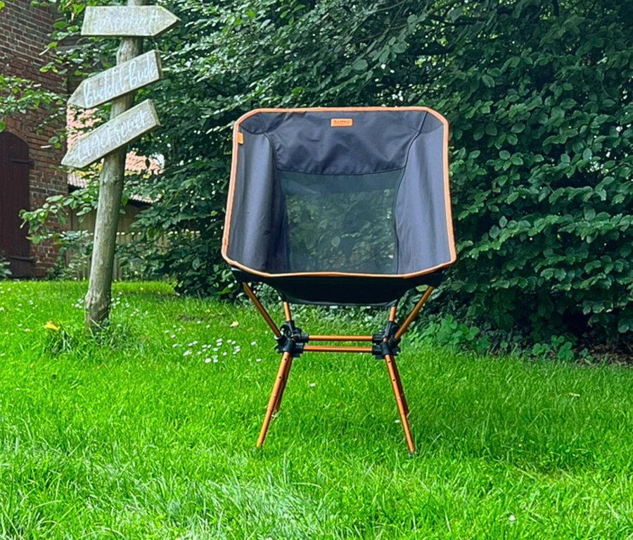Tambu Campingstuhl »BATASA COMFORT« steht auf einer Wiese vor einem Baum und einem Wegweiser.