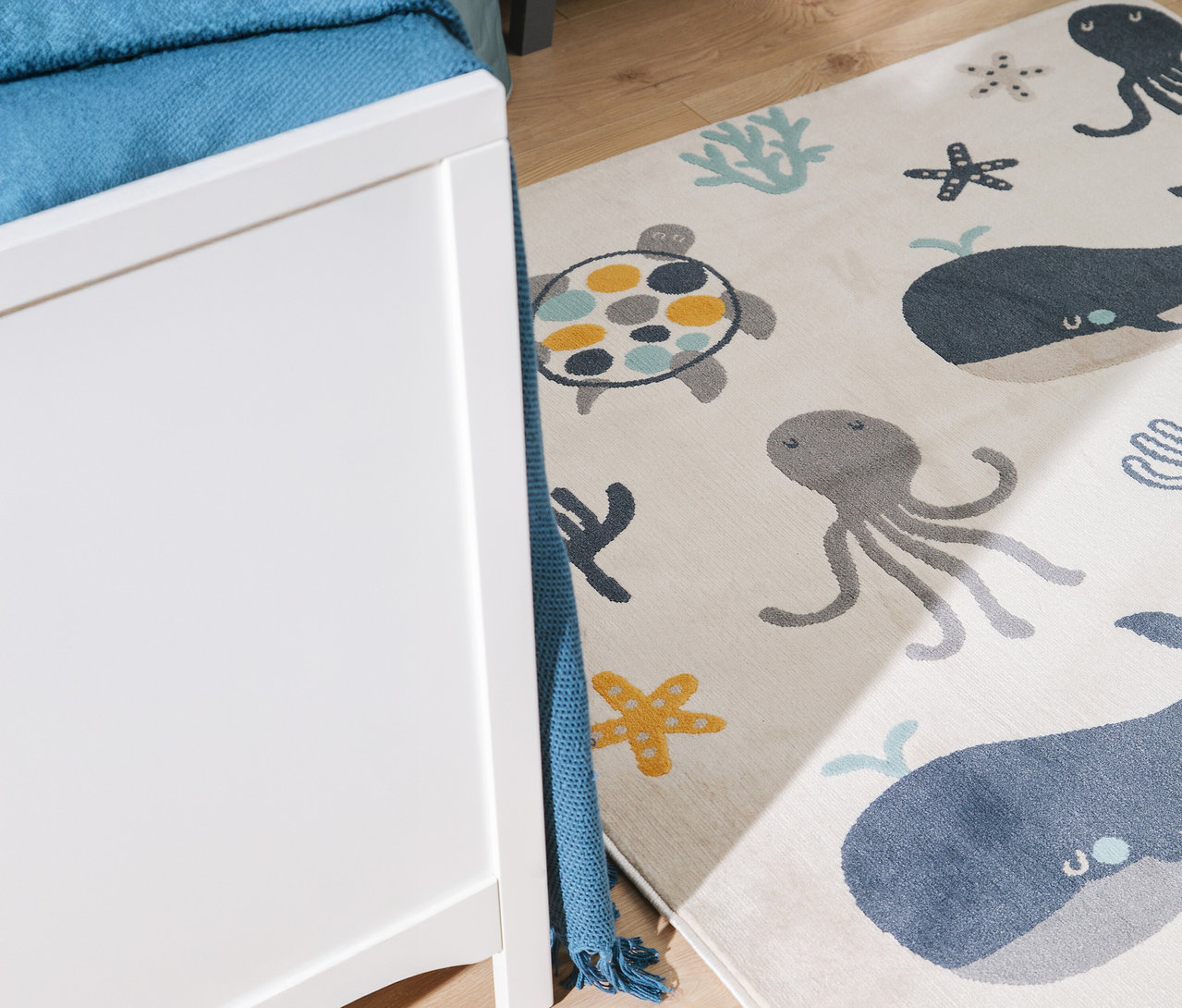 Ein Kinderzimmerteppich mit Meeresmotiven liegt neben einem weißen Möbelstück.